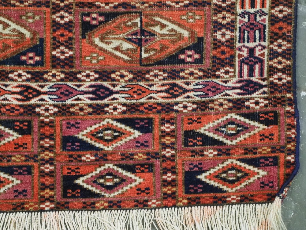 A hand-knotted wool Tekke Turkmen chuval face with repeating geometric aina gul motifs in red, navy blue, and ivory tones, finished with a fringed lower border. View X