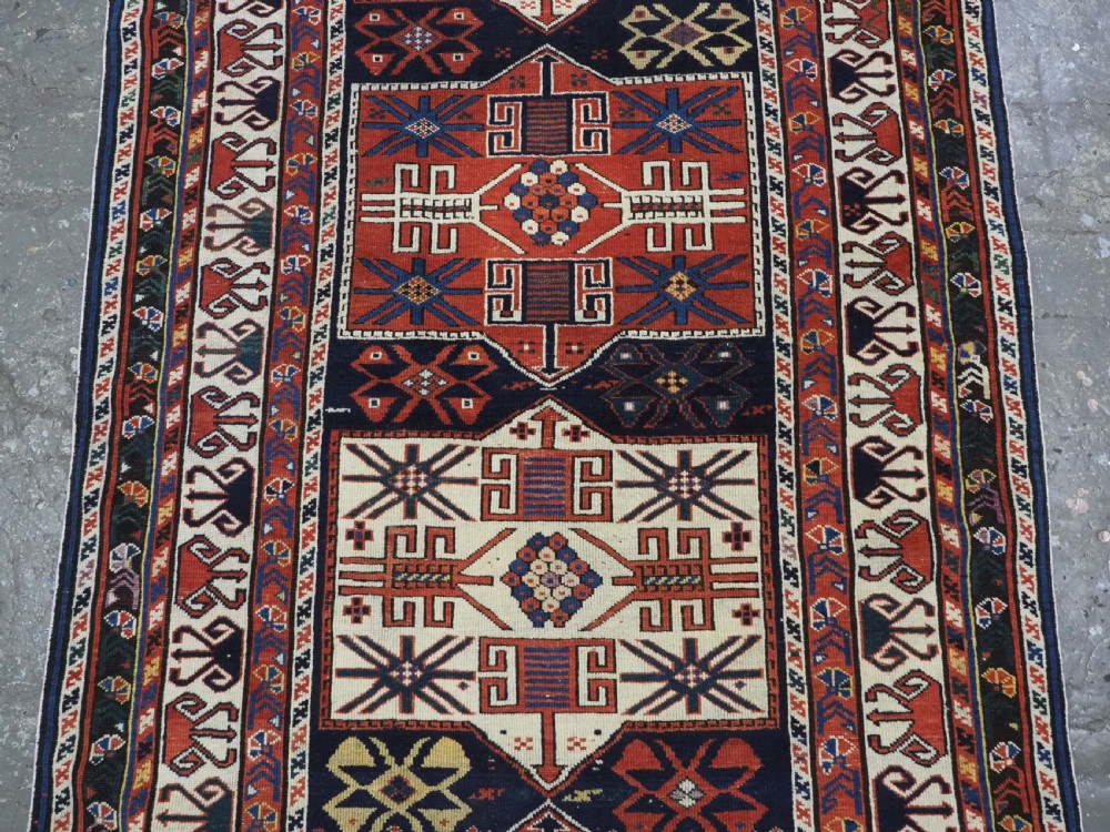 An antique hand-knotted Caucasian Shirvan wool rug featuring geometric stepped medallions on a deep blue field with red and cream patterned borders. View III