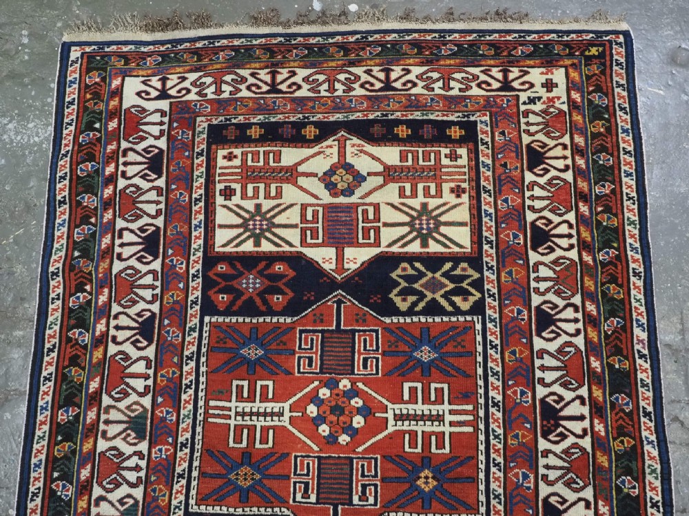 An antique hand-knotted Caucasian Shirvan wool rug featuring geometric stepped medallions on a deep blue field with red and cream patterned borders. View IV