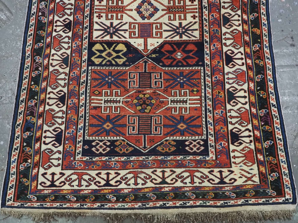 An antique hand-knotted Caucasian Shirvan wool rug featuring geometric stepped medallions on a deep blue field with red and cream patterned borders. View V