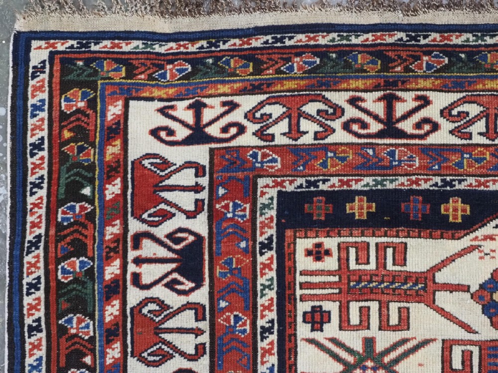 An antique hand-knotted Caucasian Shirvan wool rug featuring geometric stepped medallions on a deep blue field with red and cream patterned borders. View VI