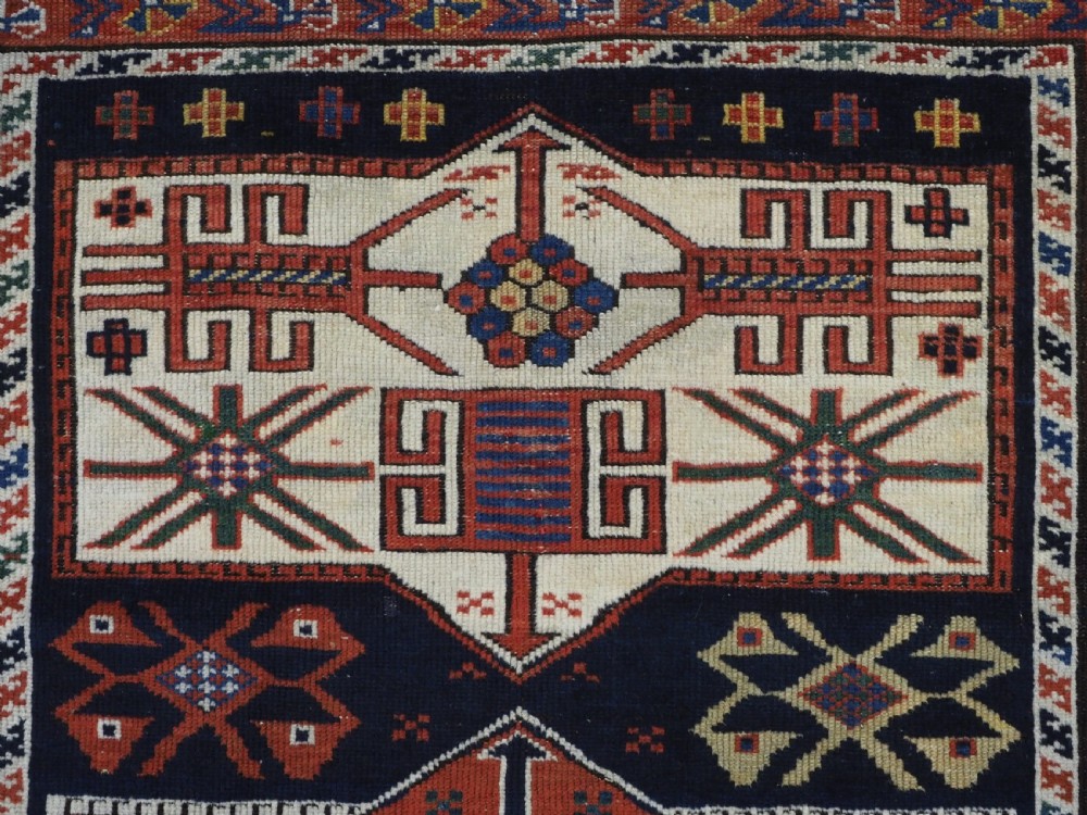 An antique hand-knotted Caucasian Shirvan wool rug featuring geometric stepped medallions on a deep blue field with red and cream patterned borders. View VIII
