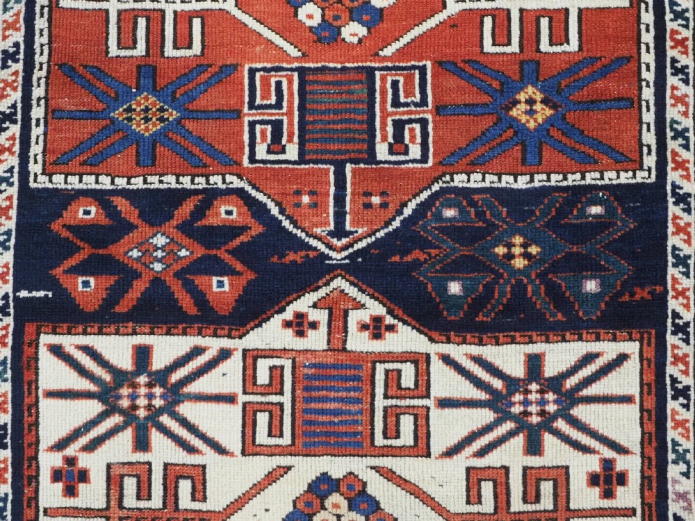 An antique hand-knotted Caucasian Shirvan wool rug featuring geometric stepped medallions on a deep blue field with red and cream patterned borders. View X