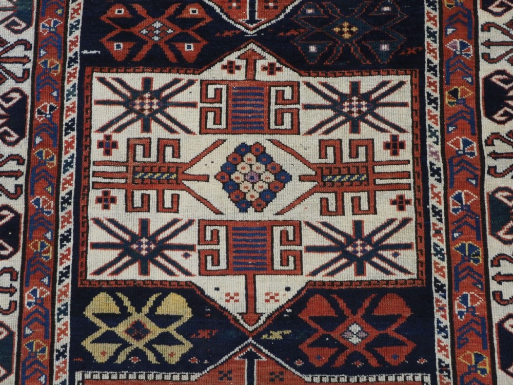 An antique hand-knotted Caucasian Shirvan wool rug featuring geometric stepped medallions on a deep blue field with red and cream patterned borders. View XI