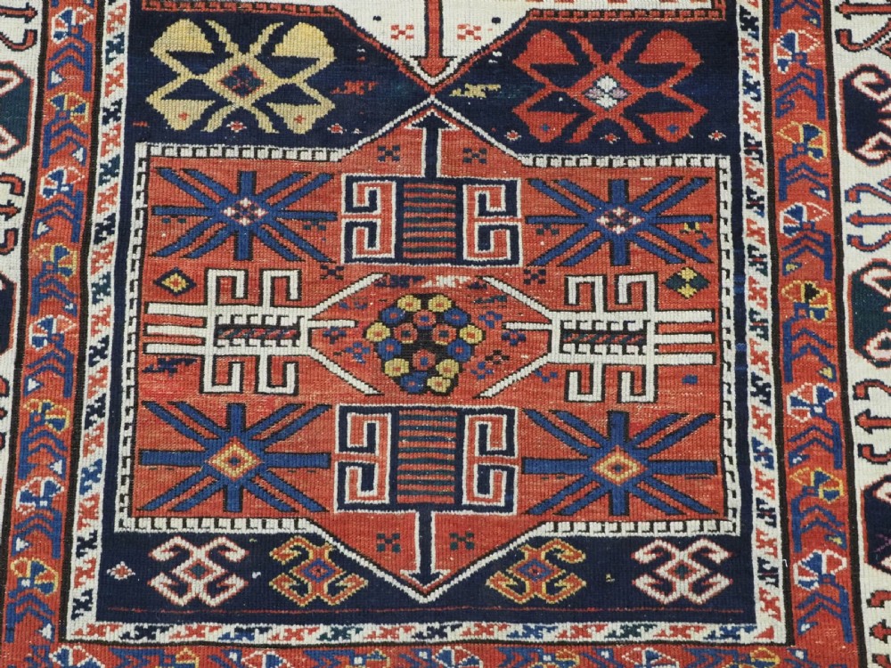 An antique hand-knotted Caucasian Shirvan wool rug featuring geometric stepped medallions on a deep blue field with red and cream patterned borders. View XII