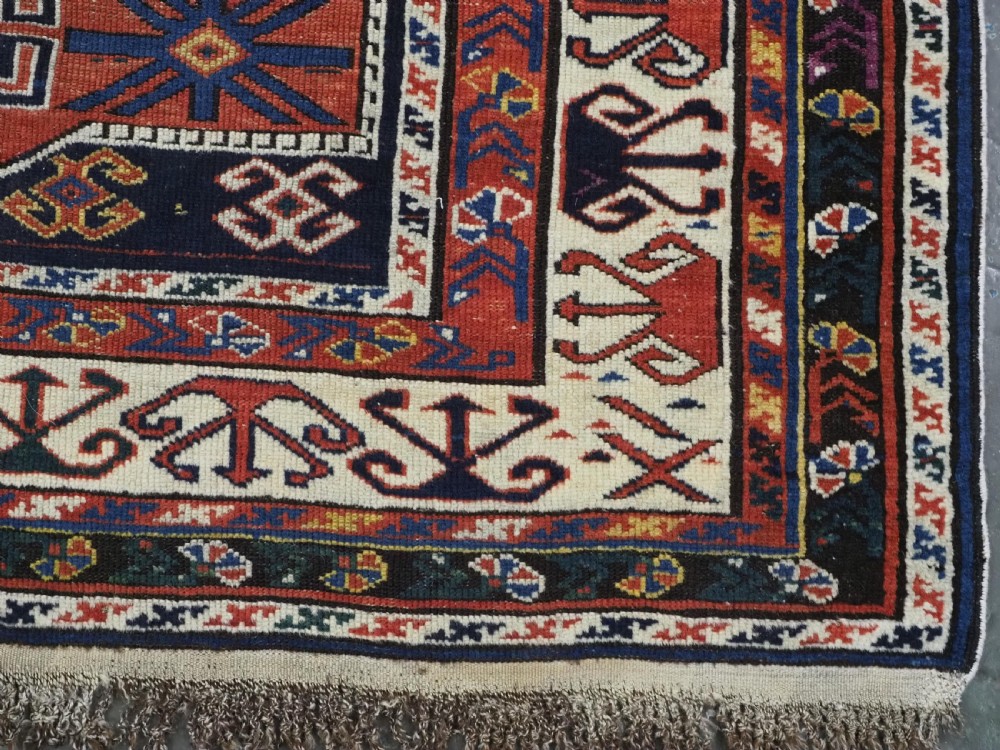 An antique hand-knotted Caucasian Shirvan wool rug featuring geometric stepped medallions on a deep blue field with red and cream patterned borders. View XIII