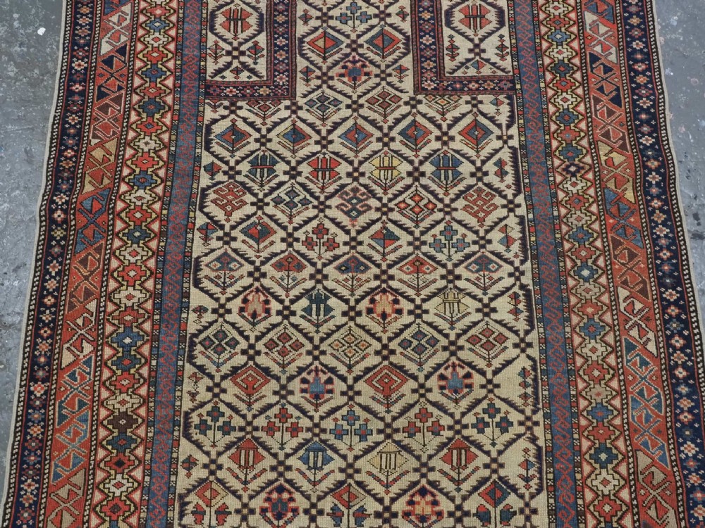 An antique Caucasian Shirvan prayer rug featuring an ivory ground decorated with a geometric floral lattice pattern and a arched mihrab. View IV