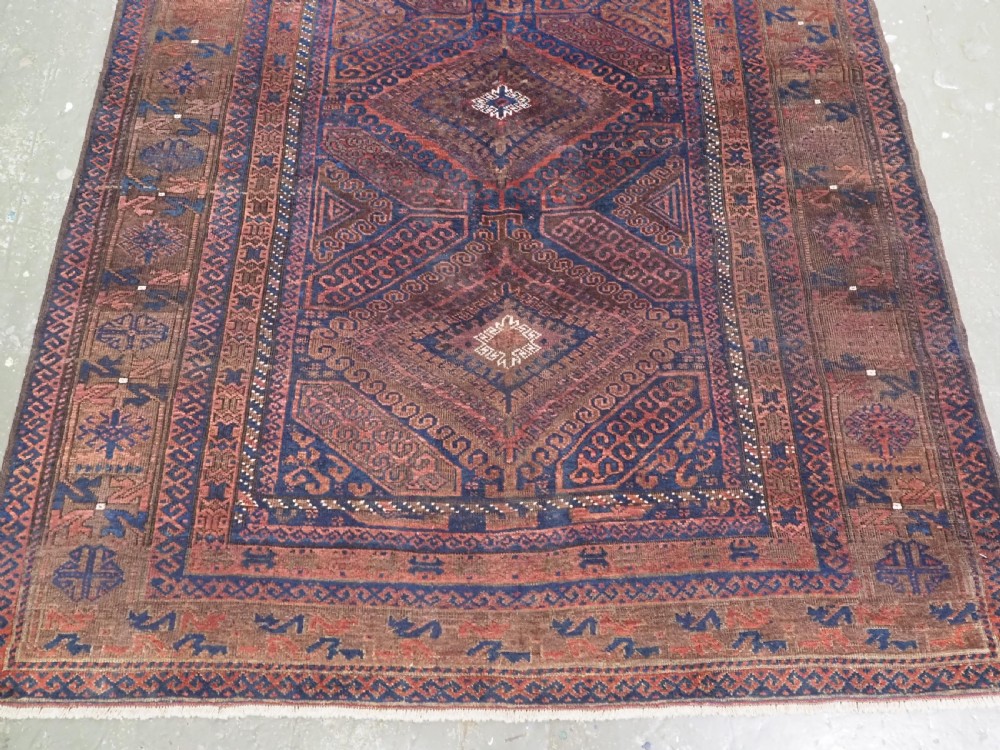 An antique hand-knotted wool carpet featuring dark brown and indigo geometric diamond medallions and detailed decorative borders. View IV