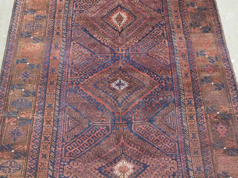 An antique hand-knotted wool carpet featuring dark brown and indigo geometric diamond medallions and detailed decorative borders. View V