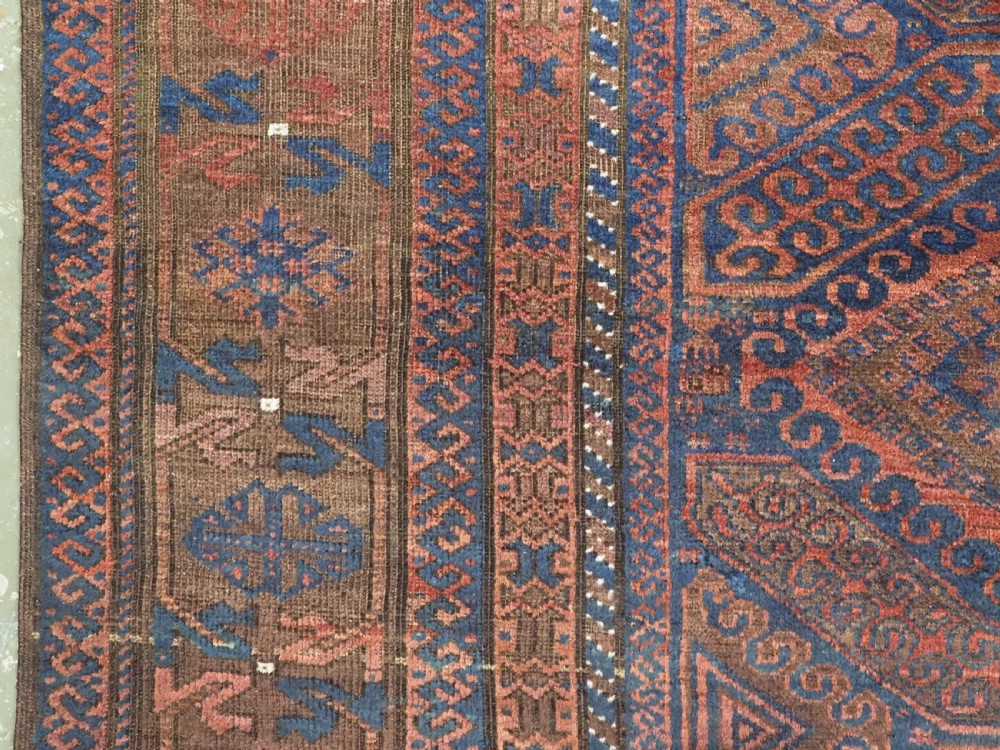 An antique hand-knotted wool carpet featuring dark brown and indigo geometric diamond medallions and detailed decorative borders. View VII