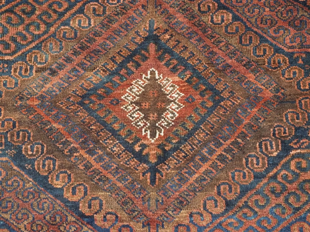 An antique hand-knotted wool carpet featuring dark brown and indigo geometric diamond medallions and detailed decorative borders. View IX