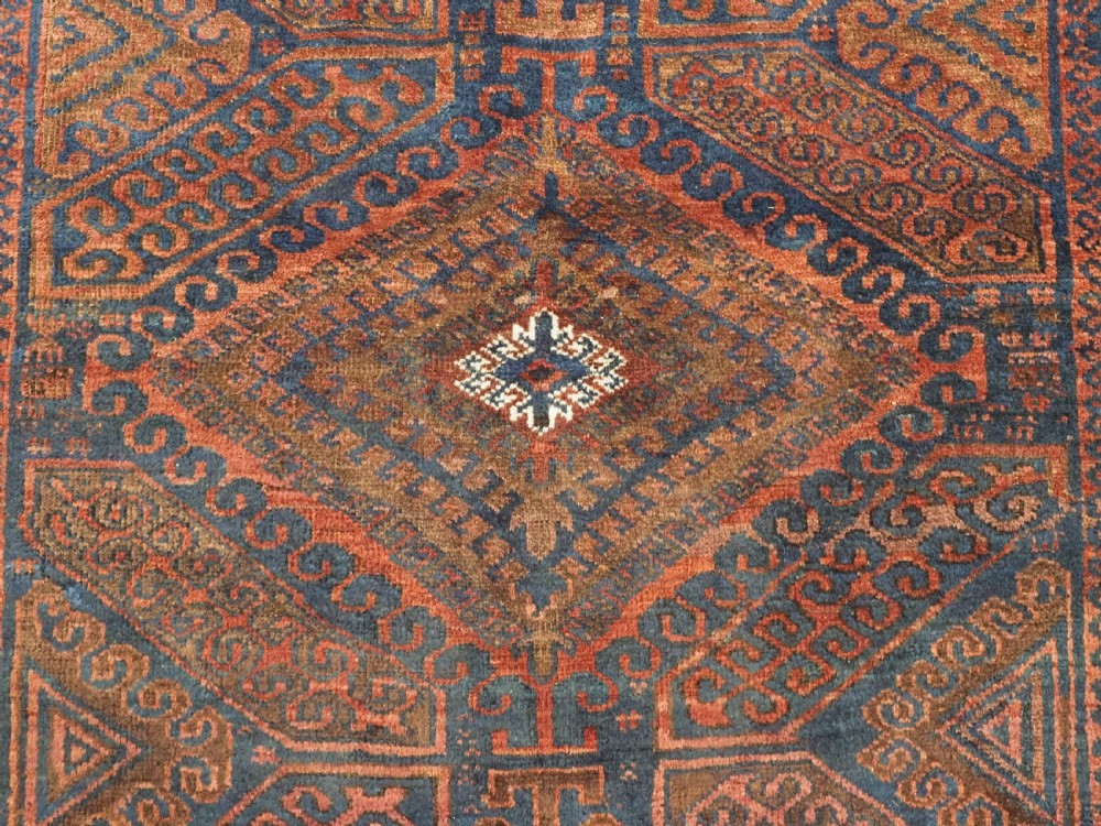 An antique hand-knotted wool carpet featuring dark brown and indigo geometric diamond medallions and detailed decorative borders. View X
