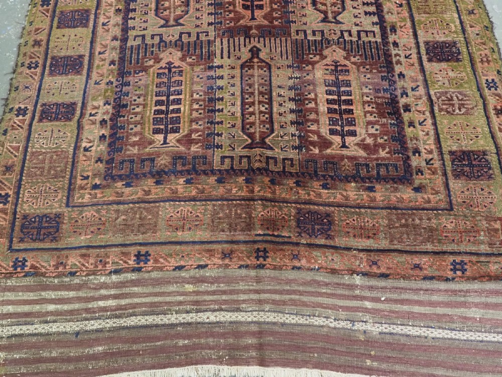 An antique hand-knotted Timuri Baluch wool carpet featuring geometric tree motifs in terracotta, indigo, and olive green hues with woven kilim borders. View V