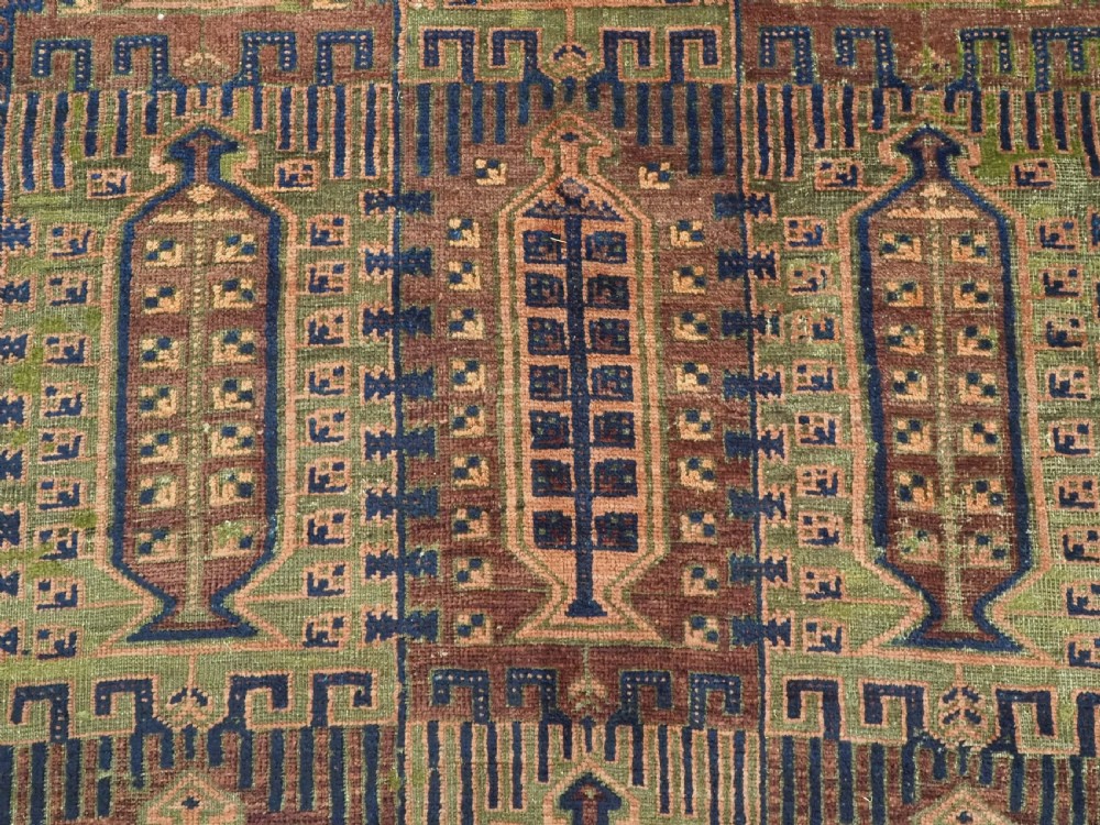 An antique hand-knotted Timuri Baluch wool carpet featuring geometric tree motifs in terracotta, indigo, and olive green hues with woven kilim borders. View IX