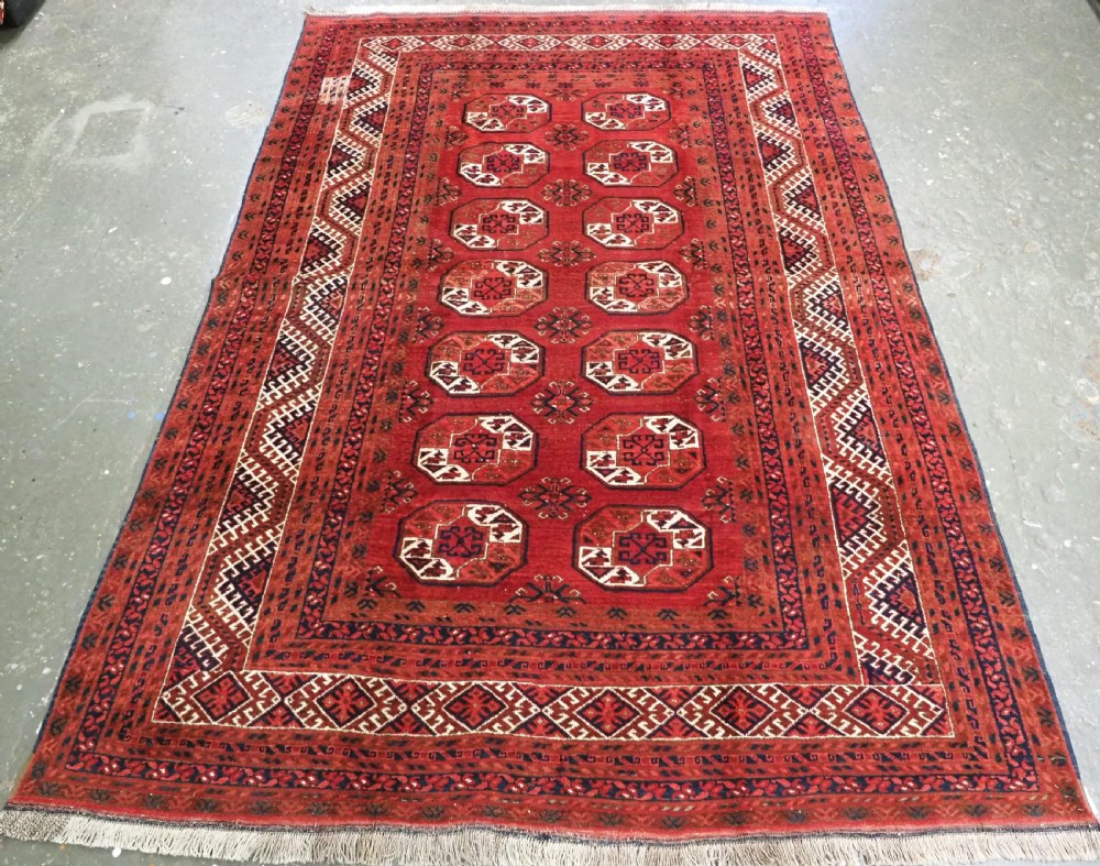 A rectangular hand-knotted wool carpet featuring a deep red field decorated with two columns of octagonal gul motifs surrounded by geometric borders.