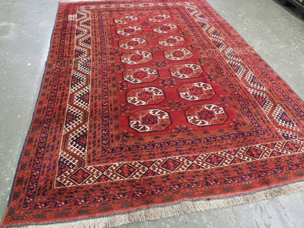 A rectangular hand-knotted wool carpet featuring a deep red field decorated with two columns of octagonal gul motifs surrounded by geometric borders. View II