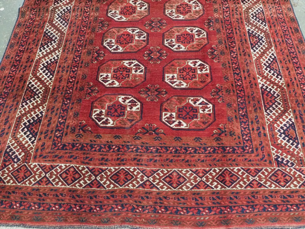 A rectangular hand-knotted wool carpet featuring a deep red field decorated with two columns of octagonal gul motifs surrounded by geometric borders. View IV