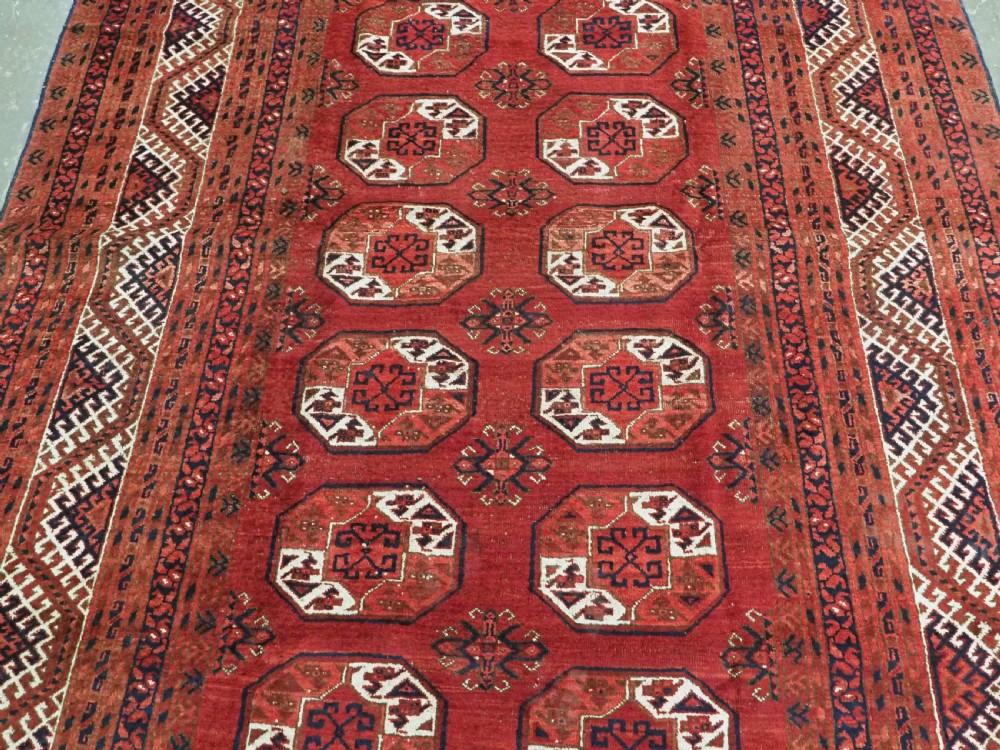 A rectangular hand-knotted wool carpet featuring a deep red field decorated with two columns of octagonal gul motifs surrounded by geometric borders. View V