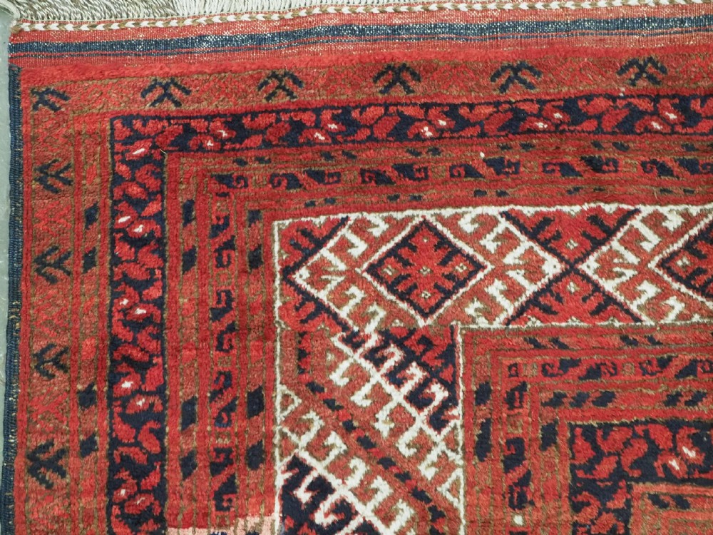 A rectangular hand-knotted wool carpet featuring a deep red field decorated with two columns of octagonal gul motifs surrounded by geometric borders. View VI