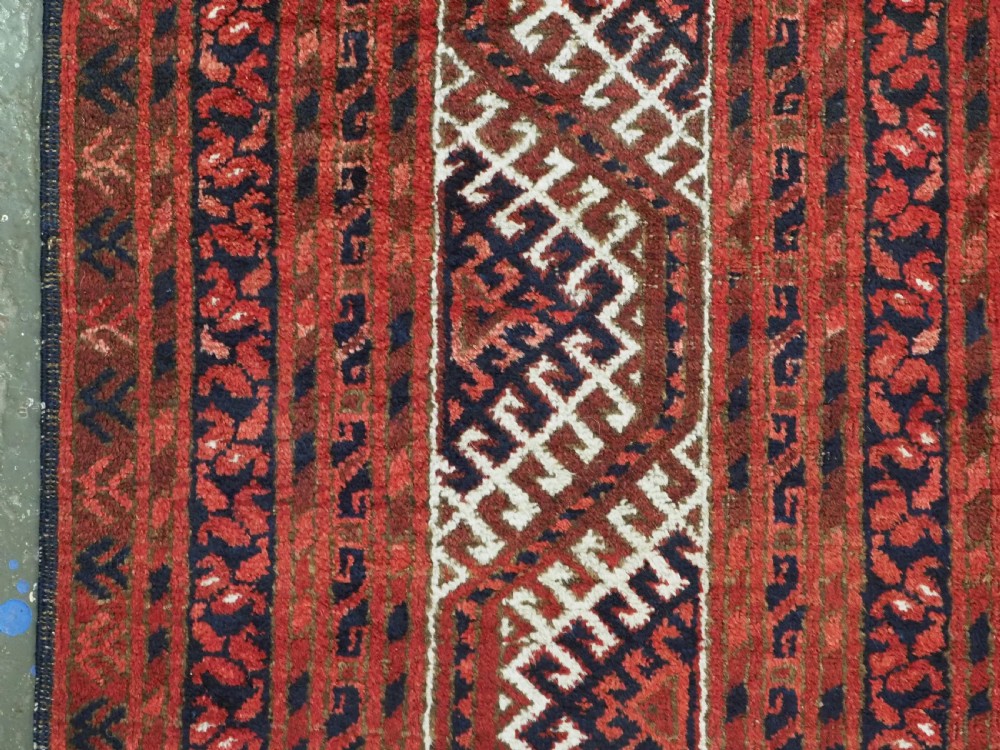 A rectangular hand-knotted wool carpet featuring a deep red field decorated with two columns of octagonal gul motifs surrounded by geometric borders. View VII