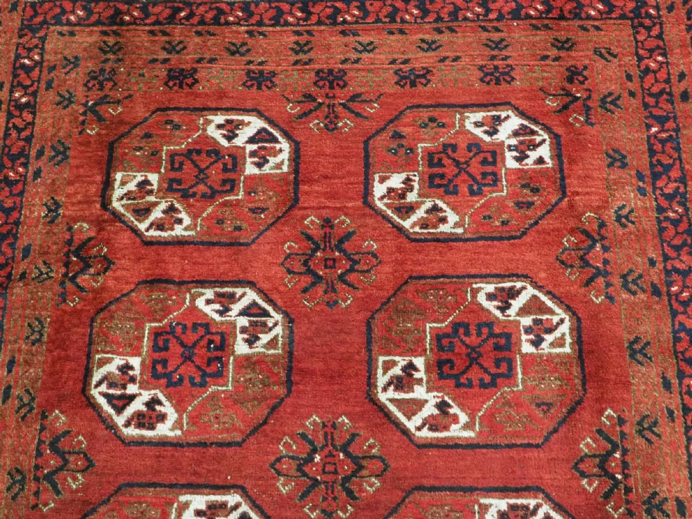 A rectangular hand-knotted wool carpet featuring a deep red field decorated with two columns of octagonal gul motifs surrounded by geometric borders. View VIII
