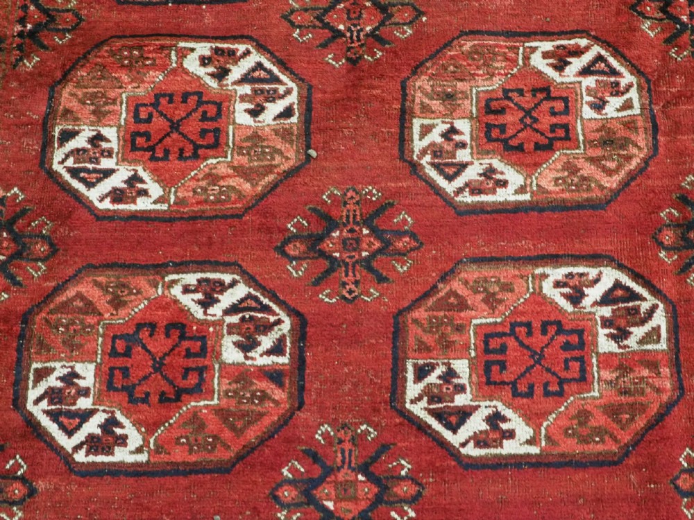 A rectangular hand-knotted wool carpet featuring a deep red field decorated with two columns of octagonal gul motifs surrounded by geometric borders. View IX