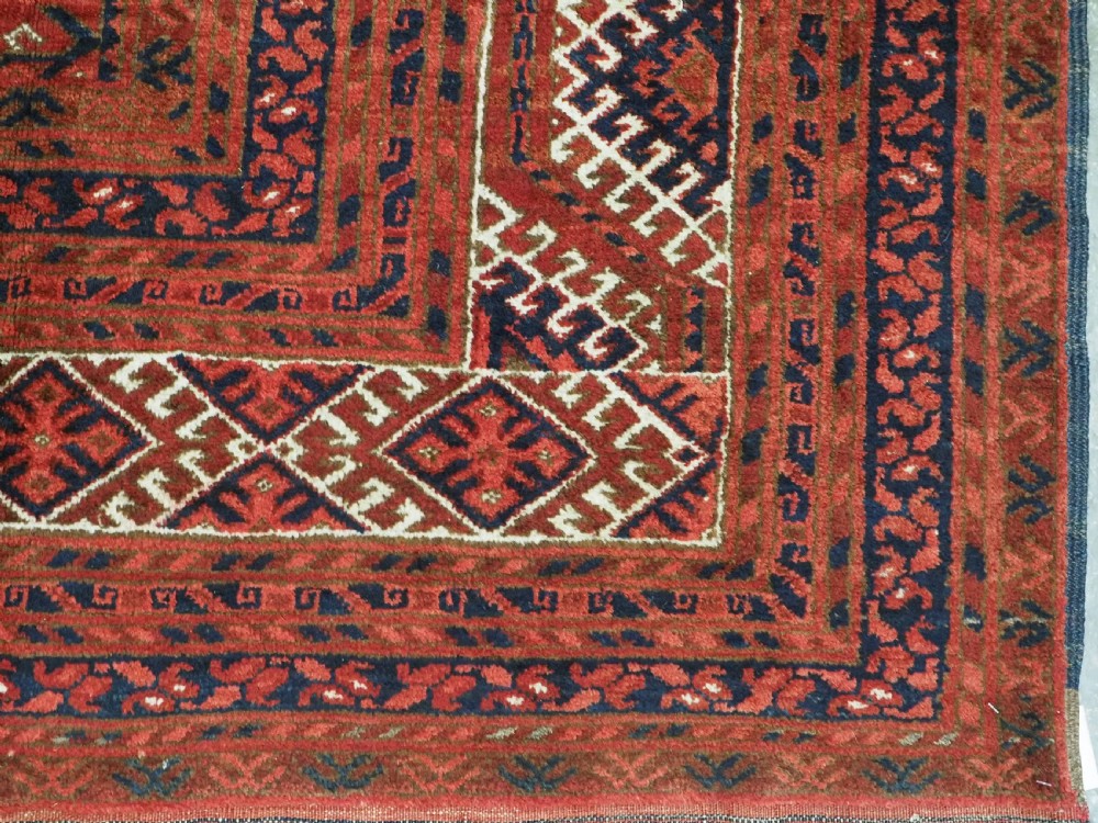 A rectangular hand-knotted wool carpet featuring a deep red field decorated with two columns of octagonal gul motifs surrounded by geometric borders. View XI