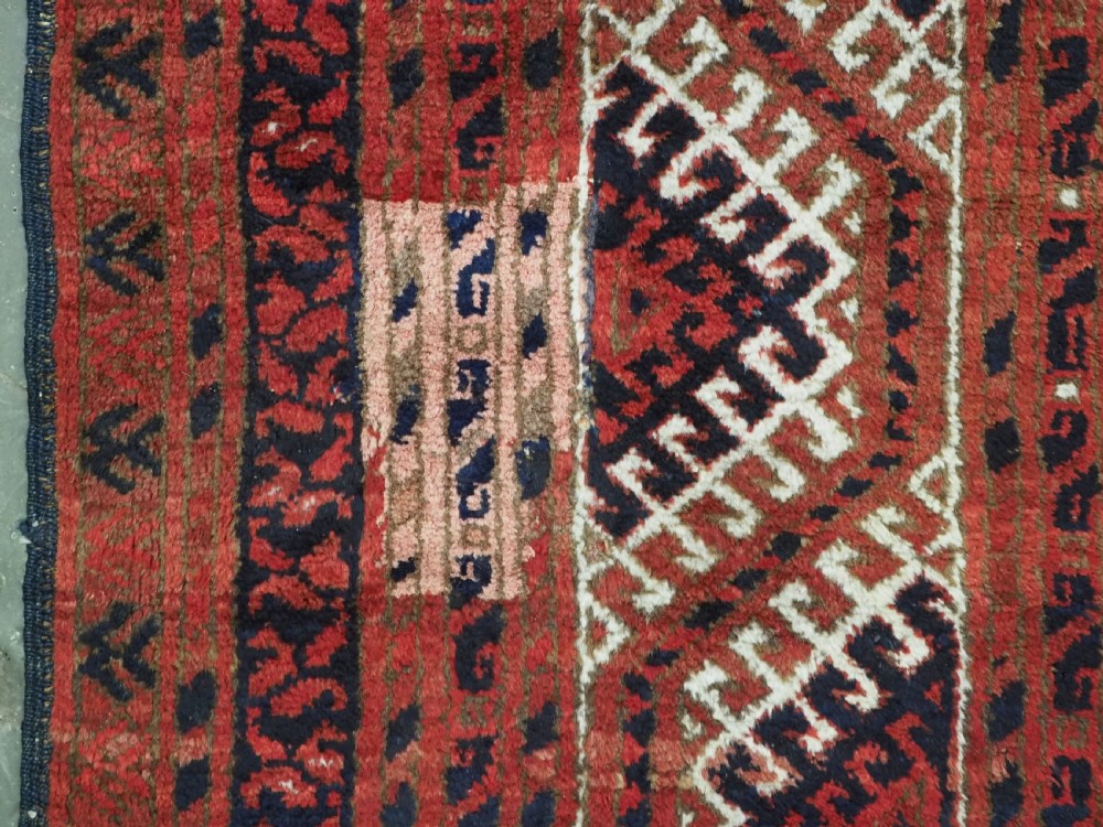 A rectangular hand-knotted wool carpet featuring a deep red field decorated with two columns of octagonal gul motifs surrounded by geometric borders. View XII