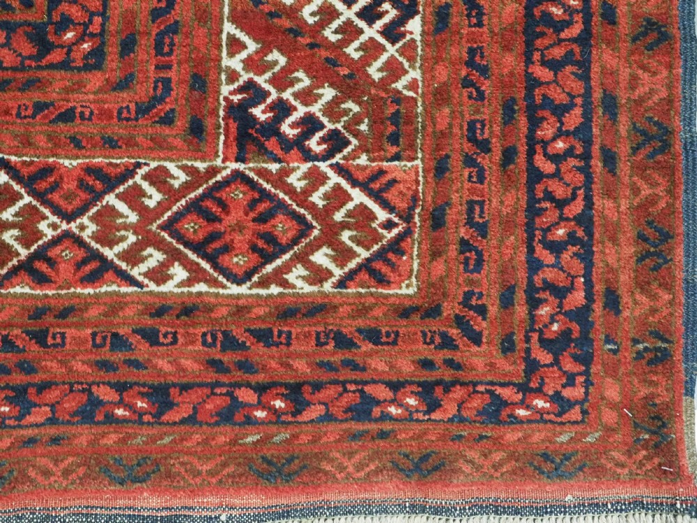 A rectangular hand-knotted wool carpet featuring a deep red field decorated with two columns of octagonal gul motifs surrounded by geometric borders. View XIII