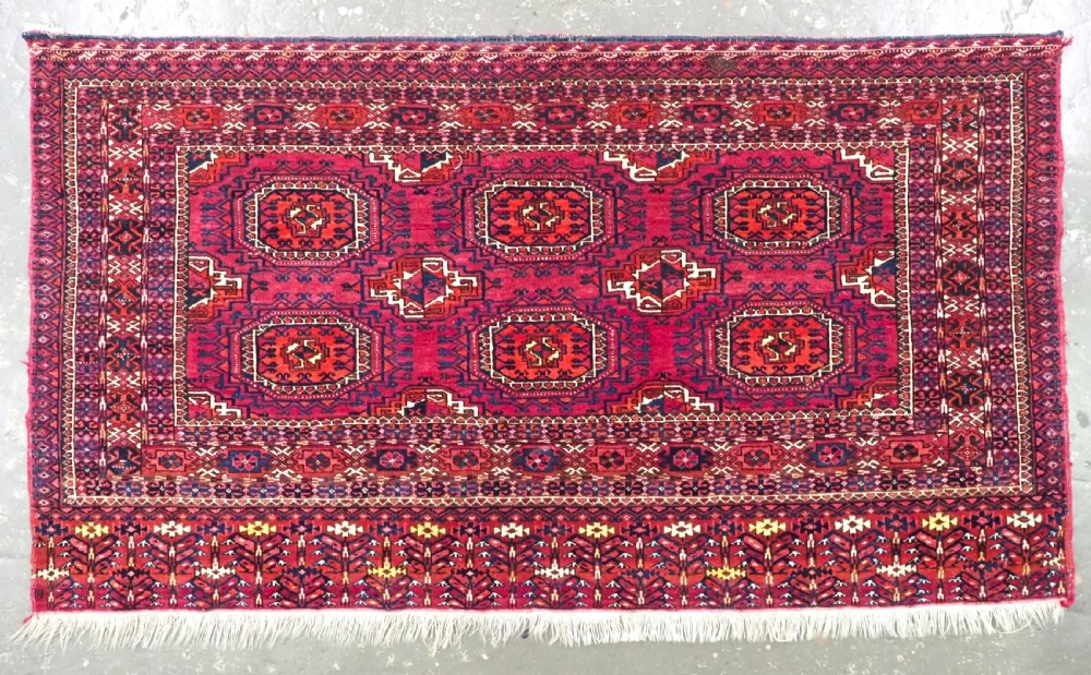 A hand-knotted crimson wool Tekke Turkmen chuval face featuring six octagonal Salor guls and geometric borders with fringe detailing.