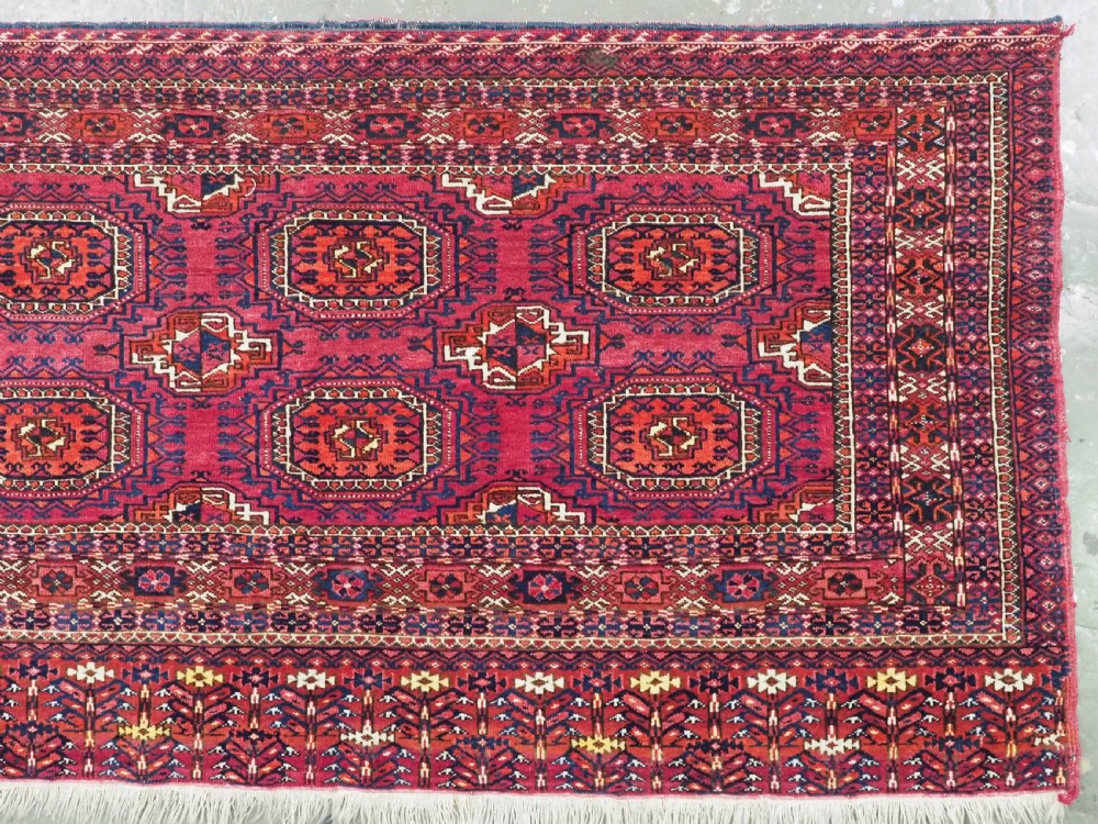 A hand-knotted crimson wool Tekke Turkmen chuval face featuring six octagonal Salor guls and geometric borders with fringe detailing. View III