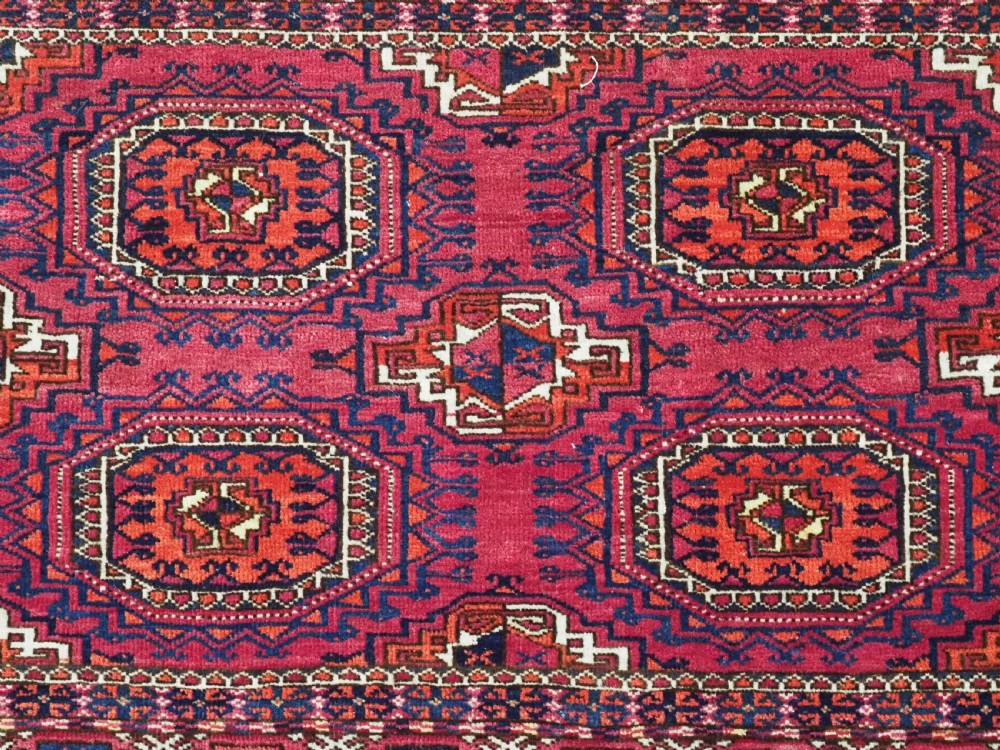 A hand-knotted crimson wool Tekke Turkmen chuval face featuring six octagonal Salor guls and geometric borders with fringe detailing. View VI