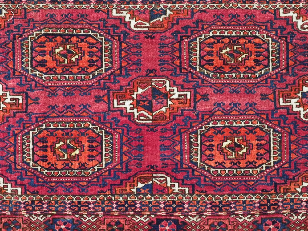 A hand-knotted crimson wool Tekke Turkmen chuval face featuring six octagonal Salor guls and geometric borders with fringe detailing. View VIII