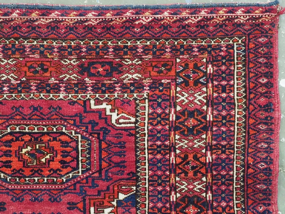 A hand-knotted crimson wool Tekke Turkmen chuval face featuring six octagonal Salor guls and geometric borders with fringe detailing. View X