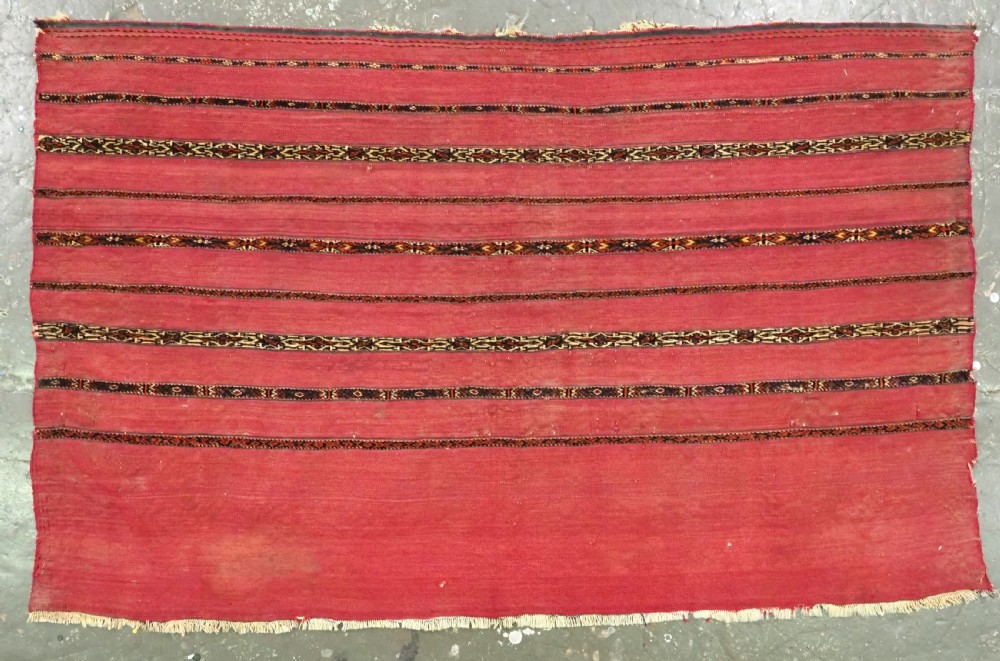A horizontal rectangular antique Tekke Turkmen Kizil chuval face textile woven in red wool with dark geometric striped bands.