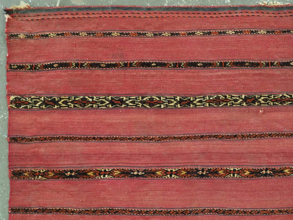 A horizontal rectangular antique Tekke Turkmen Kizil chuval face textile woven in red wool with dark geometric striped bands. View II
