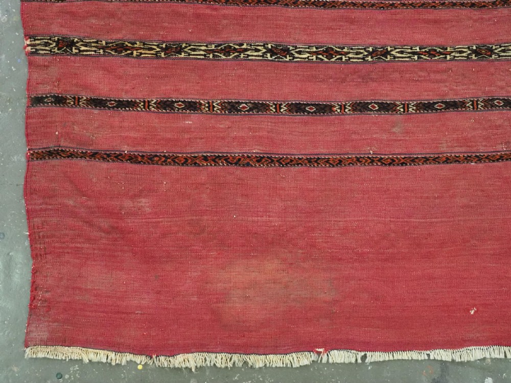 A horizontal rectangular antique Tekke Turkmen Kizil chuval face textile woven in red wool with dark geometric striped bands. View III