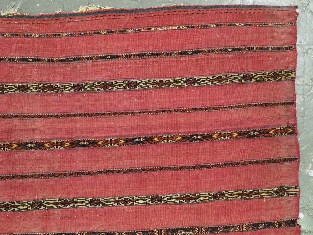 A horizontal rectangular antique Tekke Turkmen Kizil chuval face textile woven in red wool with dark geometric striped bands. View IV