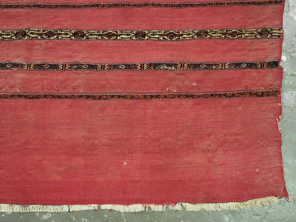 A horizontal rectangular antique Tekke Turkmen Kizil chuval face textile woven in red wool with dark geometric striped bands. View V