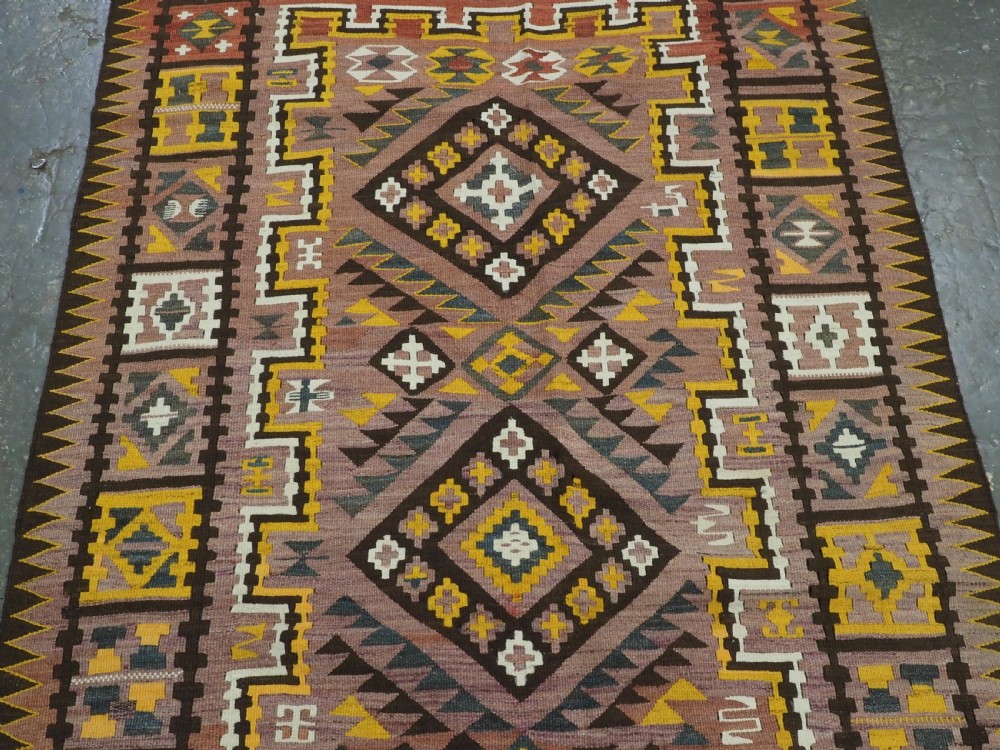A long flat-woven Afghan kilim runner carpet featuring geometric diamond motifs in terracotta, brown, yellow, and ivory shades with a tasseled fringe. View IV