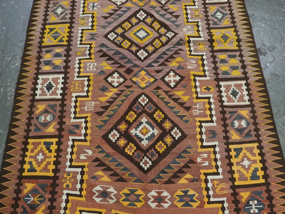 A long flat-woven Afghan kilim runner carpet featuring geometric diamond motifs in terracotta, brown, yellow, and ivory shades with a tasseled fringe. View V