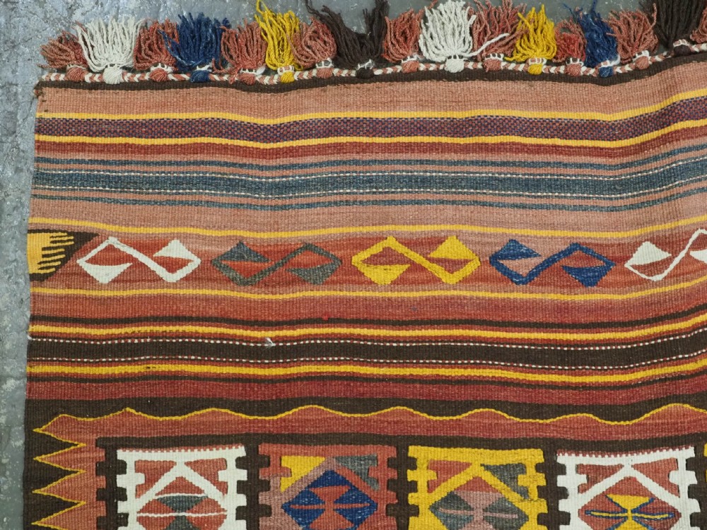A long flat-woven Afghan kilim runner carpet featuring geometric diamond motifs in terracotta, brown, yellow, and ivory shades with a tasseled fringe. View VII