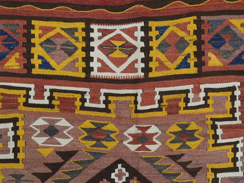 A long flat-woven Afghan kilim runner carpet featuring geometric diamond motifs in terracotta, brown, yellow, and ivory shades with a tasseled fringe. View IX