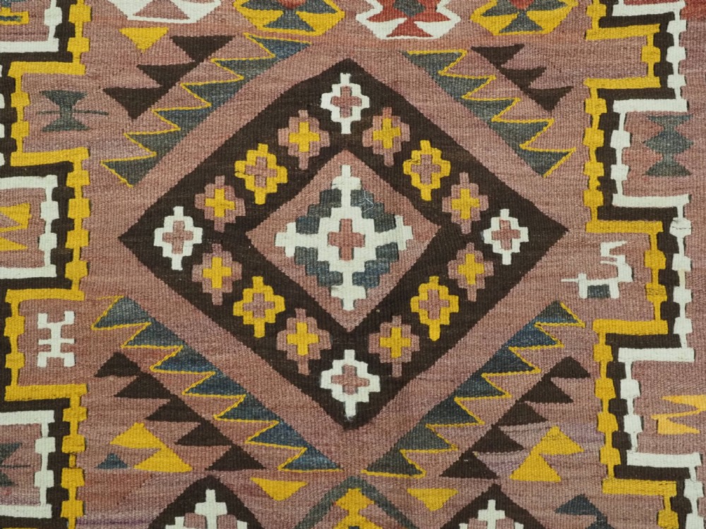 A long flat-woven Afghan kilim runner carpet featuring geometric diamond motifs in terracotta, brown, yellow, and ivory shades with a tasseled fringe. View X