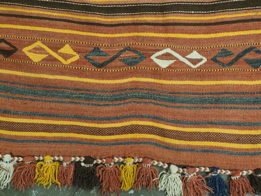 A long flat-woven Afghan kilim runner carpet featuring geometric diamond motifs in terracotta, brown, yellow, and ivory shades with a tasseled fringe. View XII