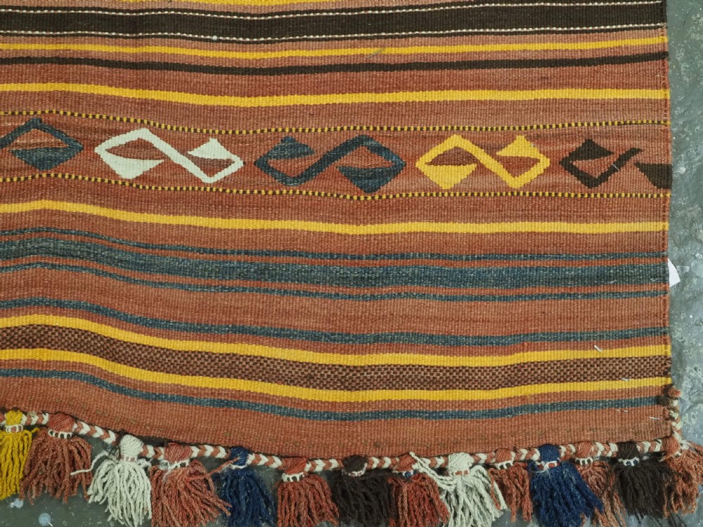 A long flat-woven Afghan kilim runner carpet featuring geometric diamond motifs in terracotta, brown, yellow, and ivory shades with a tasseled fringe. View XIII
