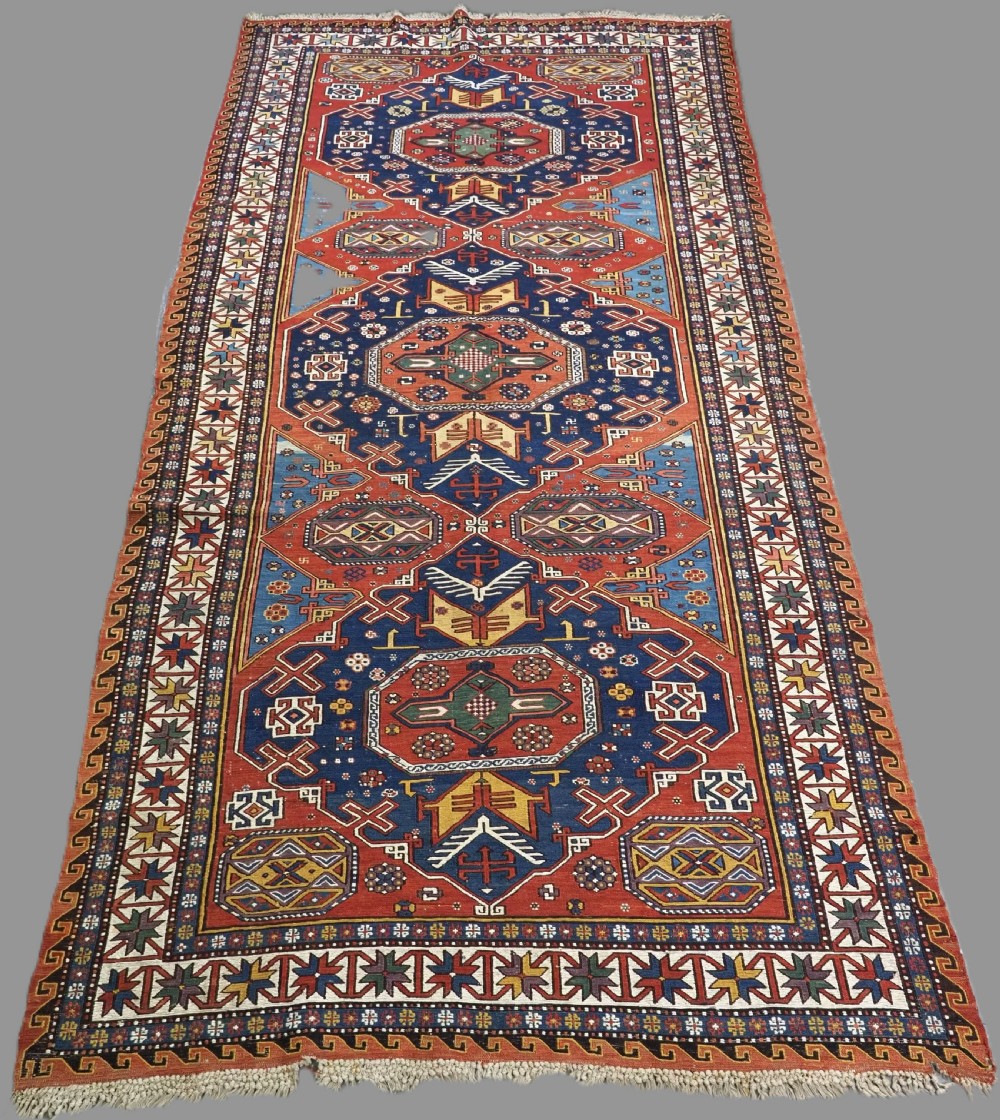 An antique Caucasian Soumak wool flatweave rug featuring three central octagonal medallions surrounded by geometric tribal motifs in red, blue, and yellow.