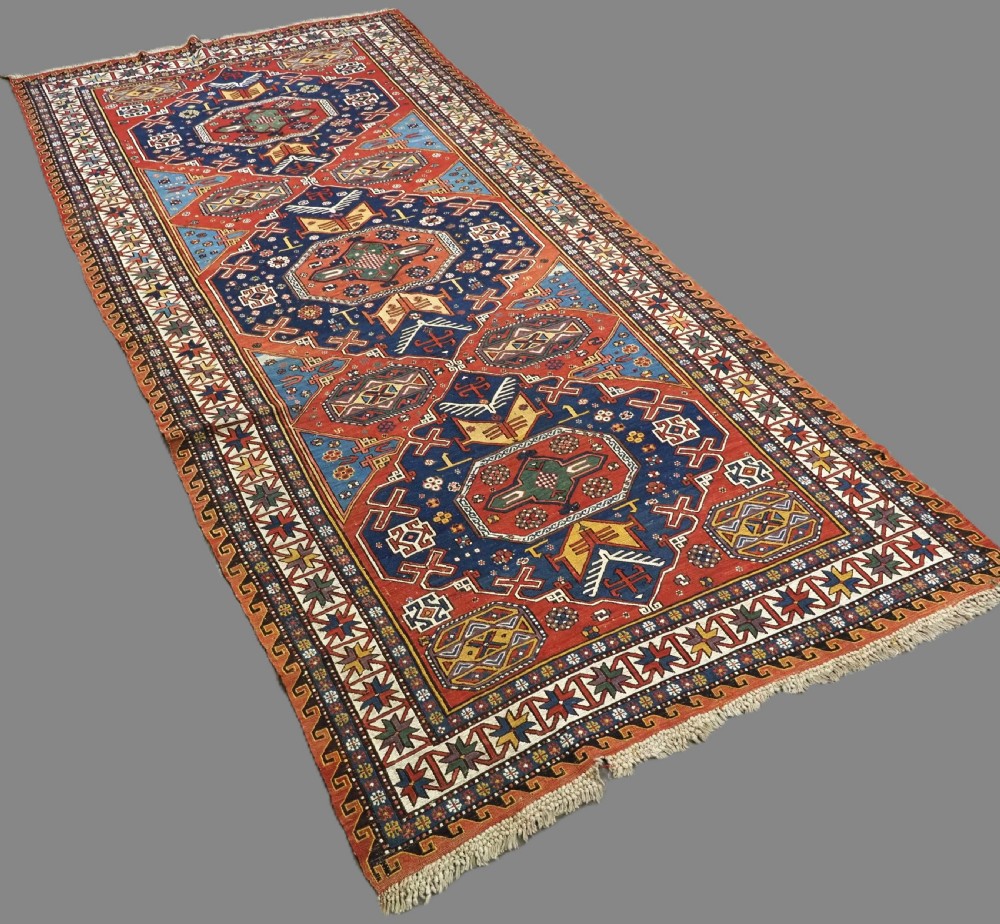 An antique Caucasian Soumak wool flatweave rug featuring three central octagonal medallions surrounded by geometric tribal motifs in red, blue, and yellow. View II