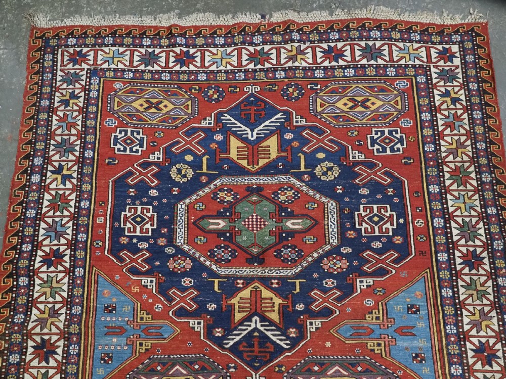 An antique Caucasian Soumak wool flatweave rug featuring three central octagonal medallions surrounded by geometric tribal motifs in red, blue, and yellow. View III