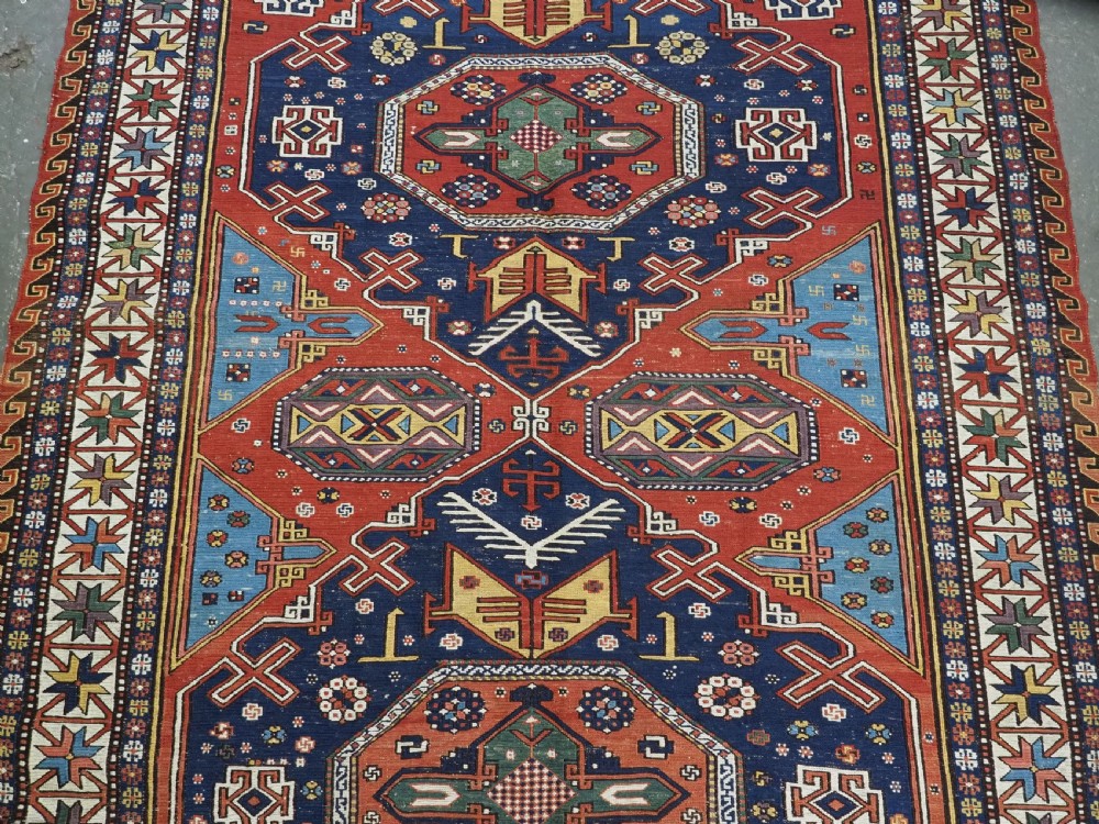 An antique Caucasian Soumak wool flatweave rug featuring three central octagonal medallions surrounded by geometric tribal motifs in red, blue, and yellow. View IV